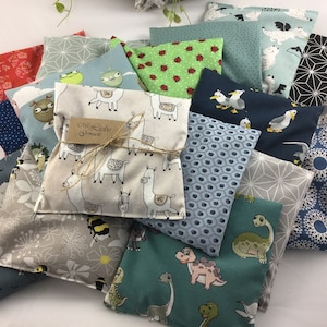 Könnte beinhalten: Eine Sammlung bunter Stoffbeutel mit verschiedenen Mustern, darunter Lamas, Enten, geometrische Muster und Dinosaurier. Die Beutel sind aus weichen, natürlichen Stoffen gefertigt und eignen sich perfekt zum Verstauen kleiner Gegenstände.