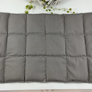 Könnte beinhalten: Ein rechteckiges, gepolstertes Kissen mit einem grau-weiß gestreiften Muster. Das Kissen ist in mehrere rechteckige Abschnitte unterteilt. Auf der linken Seite ist ein kleines schwarzes Etikett zu sehen. Das Kissen liegt auf einer weißen Oberfläche.