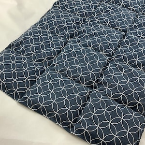 Könnte beinhalten: Ein marineblaues, gestepptes Pad mit weißem geometrischen Muster. Das Pad ist rechteckig mit einer Reihe von aufgenähten Quadraten. Der Stoff hat ein sich wiederholendes Design aus ineinandergreifenden Kreisen. Das Etikett "ElizabethDesign" ist sichtbar.