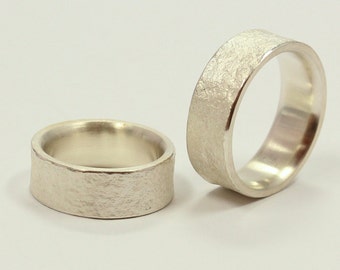 May include: Two silver wedding bands with a textured finish. The bands are wide and have a rounded profile.