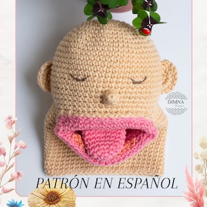 Peut inclure: Une poupée amigurumi en crochet avec une bouche et une langue roses, les yeux fermés et une tête beige. La poupée est posée sur une surface blanche. Le texte "PATRÓN EN ESPAÑOL" est en bas de l'image.