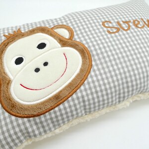 May include: A rectangular pillow with a gray and white gingham pattern. The pillow features a large, embroidered monkey face in shades of brown, cream, and black. The name "Sven" is embroidered in brown. The pillow has a soft, cream-colored border.
