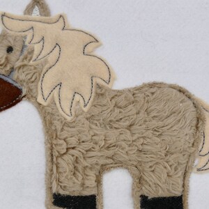 Könnte beinhalten: Ein braunes und beiges Plüschpferd mit einer braunen Filznase und schwarzen Filzhufen. Das Pferd hat eine beige Filzmähne und einen Filzschwanz.