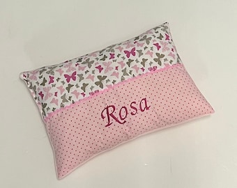 Op de afbeelding: Een roze en wit kussen met een vlinderpatroon aan de ene kant en roze stippen aan de andere kant. De naam "Rosa" is geborduurd op de kant met de stippen.
