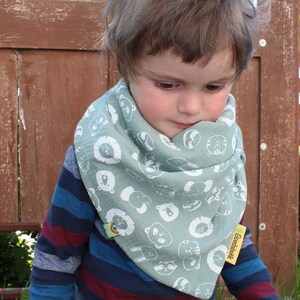 Puede incluir: Un ni&ntilde;o peque&ntilde;o con una camisa de manga larga a rayas azules y rojas con un pa&ntilde;uelo verde con caras de animales blancas y el texto "Boeddhabutik".