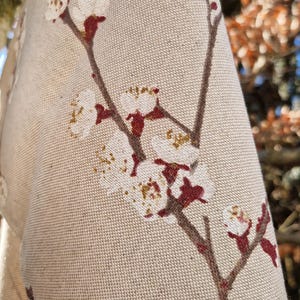 May include: A beige fabric with a floral pattern of white flowers and red stems. The fabric has a textured surface.