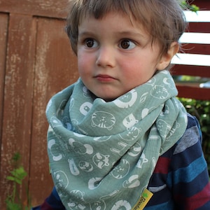 Puede incluir: Un ni&ntilde;o peque&ntilde;o con un pa&ntilde;uelo verde con estampado de animales blancos y una camisa de manga larga a rayas azules y rojas. El pa&ntilde;uelo tiene una etiqueta amarilla con el texto "Bodedunk" en ella.