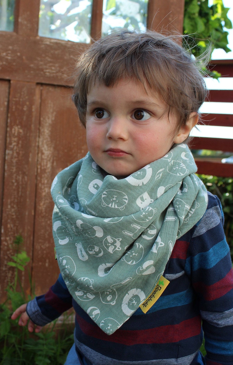 Puede incluir: Un ni&ntilde;o peque&ntilde;o con un pa&ntilde;uelo verde con estampado de animales blancos y una camisa de manga larga a rayas azules y rojas. El pa&ntilde;uelo tiene una etiqueta amarilla con el texto "Bodedunk" en ella.