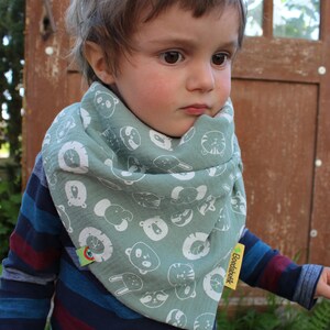 Puede incluir: Un ni&ntilde;o peque&ntilde;o con una camisa de manga larga a rayas azules y rojas con un pa&ntilde;uelo verde con estampado de animales blancos. El pa&ntilde;uelo tiene una etiqueta amarilla que dice "Boedabatik".