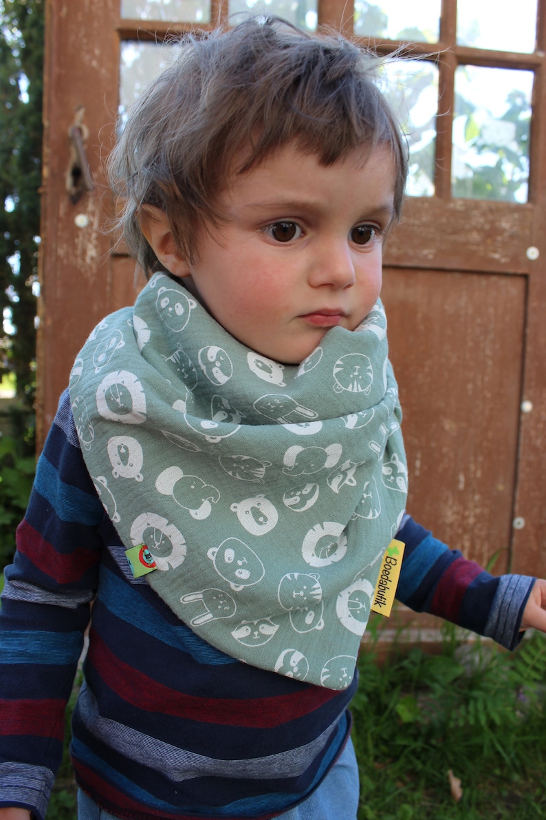 Puede incluir: Un ni&ntilde;o peque&ntilde;o con una camisa de manga larga a rayas azules y rojas con un pa&ntilde;uelo verde con estampado de animales blancos. El pa&ntilde;uelo tiene una etiqueta amarilla que dice "Boedabatik".