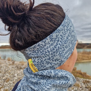 Könnte beinhalten: Hellblaues Stirnband und Halstuch-Set mit marineblauem Blättermuster. Das Stirnband wird auf dem Kopf getragen, das Halstuch um den Hals. Ein gelbes Etikett mit dem Text "Goedabubi" ist am Halstuch befestigt.