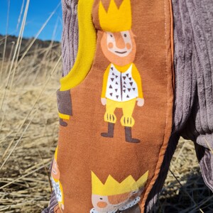 May include: Brown corduroy pants with a yellow waistband and a pattern of cartoon kings wearing gold crowns. The fabric has a textured, corduroy look.