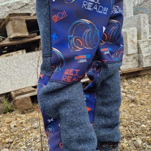 May include: Gaming-themed trousers in blue and grey, with a navy blue background displaying a controller, headphones, and the words "GET READY" and "GO!!". The trousers have grey cuffs and are worn with blue hiking boots.