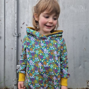 May include: A child wearing a teal blue hooded sweatshirt with a colourful floral pattern. The sweatshirt has yellow trim around the hood and cuffs.