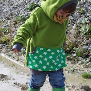May include: A child wearing a green hooded sweatshirt with a white star pattern on the pocket, blue jeans, and green and blue rain boots, standing in a muddy area.