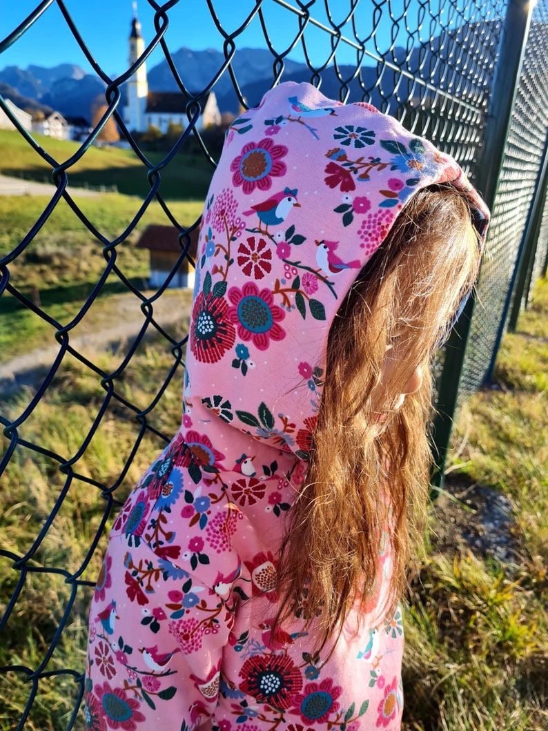 May include: A pink hooded sweatshirt with a floral and bird print. The sweatshirt is made of soft, comfortable fabric and features a drawstring hood.