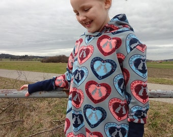 Könnte beinhalten: Ein grauer Kapuzenpullover mit einem Herzmuster, das in jedem Herz zwei Kaninchen zeigt. Die Herzen sind in Blautönen, Rosa und Rot gehalten. Der Pullover hat dunkelblaue Bündchen und einen dunkelblauen Bund.