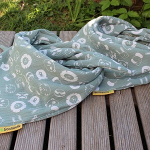 Puede incluir: Una manta de muselina verde salvia con estampado de animales blancos. La manta est&aacute; doblada y tiene una etiqueta amarilla con el texto "Boedabuik".