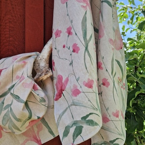 Puede incluir: Dos toallas de cocina de color crema con un estampado floral rosa y hojas verdes. Las toallas están colgadas en una pared de madera roja.