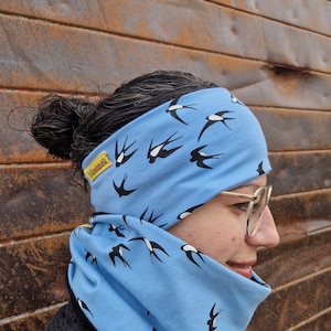 May include: A light blue neck warmer and headband set with a black swallow print. The headband has a yellow label that says "BossBabe".