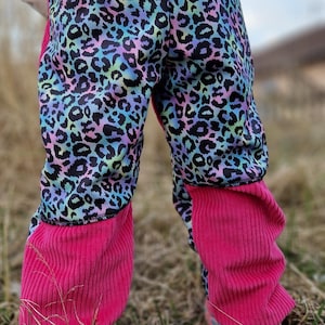 Op de afbeelding: Kleurrijke broek met een luipaardprint in blauw, paars en groen. De onderbenen zijn gemaakt van felroze corduroy stof. De broek wordt gedragen met kleurrijke sneakers.