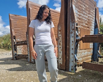 May include: A woman wearing a white t-shirt and light blue pants stands in front of a rusty metal structure. The pants have a relaxed fit and a cuffed hem.