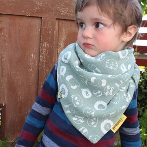 Puede incluir: Un ni&ntilde;o peque&ntilde;o con una camisa de manga larga a rayas azules y rojas y pantalones vaqueros azules. El ni&ntilde;o lleva una bandana verde con caras de animales blancas impresas. La bandana tiene una peque&ntilde;a etiqueta verde con la palabra "Boosdahik" impresa.