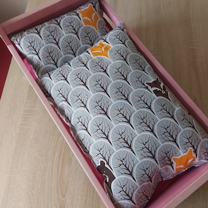 Könnte beinhalten: Ein Holz-Puppenbett mit einer rosa-weiß gestreiften Matratze. Zwei Kissen mit einem Waldtier-Druck sind auf dem Bett. Die Kissen zeigen ein Muster aus Bäumen, Füchsen und Waschbären.