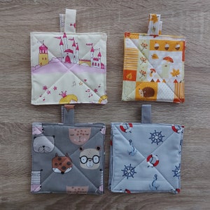 Könnte beinhalten: Vier verschiedene quadratische Topflappen mit verschiedenen Designs. Einer zeigt ein rosa Schloss auf weißem Hintergrund, ein anderer ein buntes Patchwork-Design, ein dritter einen grauen Hintergrund mit Tierillustrationen und der letzte einen blauen Hintergrund mit einem nautischen Thema.
