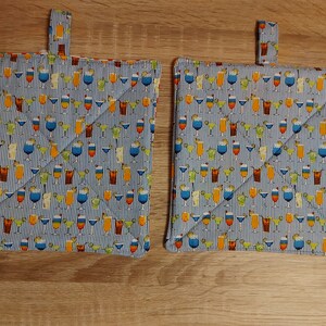 Könnte beinhalten: Zwei blaue und weiße gestreifte Topflappen mit einem Muster aus bunten Cocktails. Die Topflappen haben eine Schlaufe zum Aufhängen.