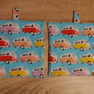 Könnte beinhalten: Zwei blaue Topflappen mit einem Muster aus bunten Vintage-Volkswagen-Transportern. Die Topflappen haben eine Schlaufe zum Aufhängen.