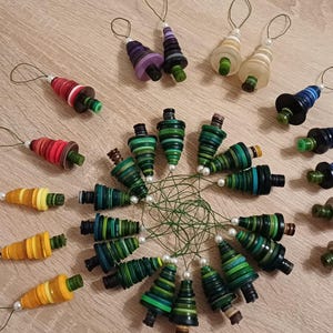 Könnte beinhalten: Eine Sammlung handgefertigter Weihnachtsschmuckstücke in verschiedenen Farben, darunter Rot, Grün, Gelb und Blau. Jedes Schmuckstück hat eine Schlaufe zum Aufhängen und ist auf einer Holzoberfläche angeordnet. Die Schmuckstücke sind kegelförmig und scheinen aus Papier zu sein.