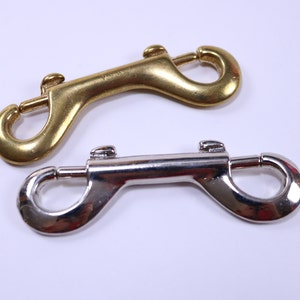 May include: Two metal snap hooks, one gold and one silver. Both hooks have a double-ended design with a spring-loaded latch.