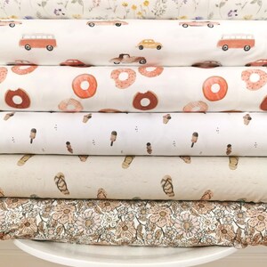 May include: A stack of six different fabric swatches with various patterns, including floral, cars, donuts, ice cream cones, sandals, and a floral pattern. The swatches are stacked on a white stool with wooden legs.