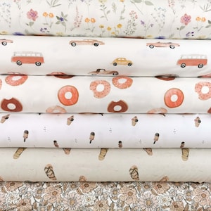 May include: Six rolls of fabric with different patterns. The top roll has a white background with small pink, yellow, and green flowers. The second roll has a white background with red and yellow cars and a red van. The third roll has a white background with pink donuts. The fourth roll has a white background with brown ice cream cones. The fifth roll has a white background with brown sandals. The bottom roll has a white background with small pink, yellow, and green flowers.