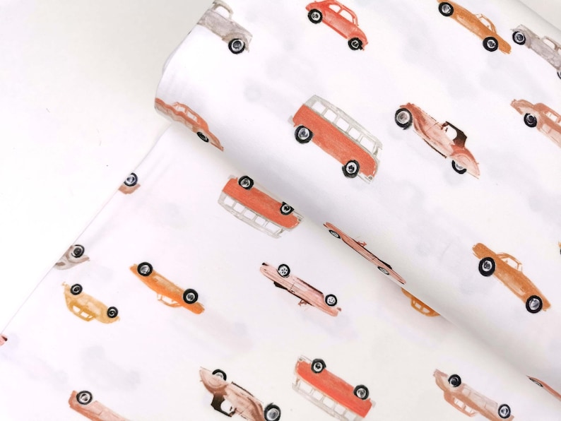 May include: White fabric with a repeating pattern of vintage cars and vans in shades of orange, red, and brown. The cars are all facing the same direction and have a whimsical, hand-painted look.