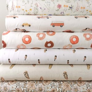 May include: A stack of six different fabric swatches with various patterns. The patterns include floral, donuts, ice cream cones, flip flops, and cars. The fabrics are all white with colored designs.