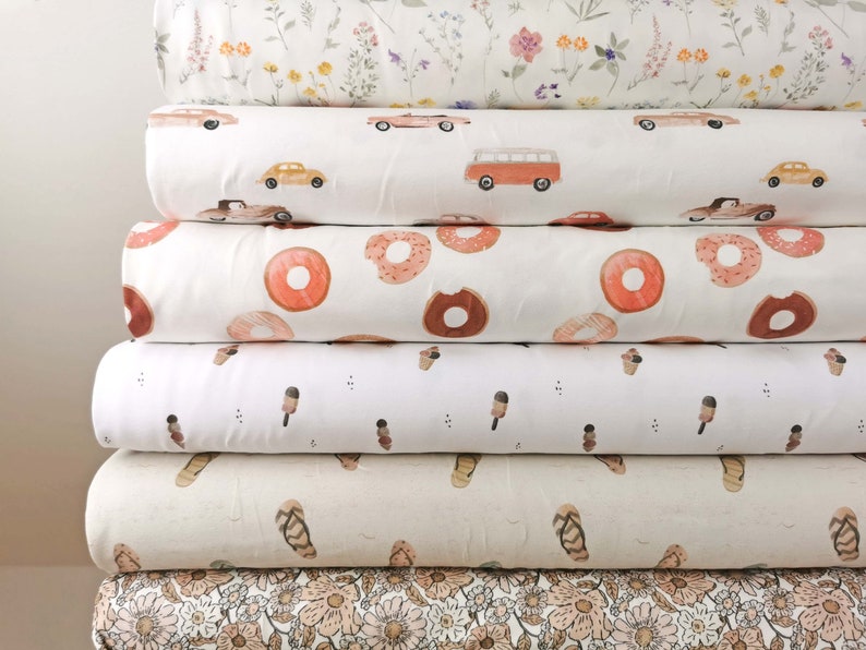 May include: A stack of six different fabric swatches with various patterns. The patterns include floral, donuts, ice cream cones, flip flops, and cars. The fabrics are all white with colored designs.