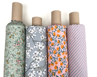 May include: Four rolls of fabric with different patterns. The first roll has a green background with small white and brown floral designs. The second roll has a light blue background with white floral designs. The third roll has a pink background with orange citrus fruit designs. The fourth roll has a pink and gray striped pattern.