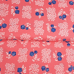 Könnte beinhalten: Korallenfarbener Stoff mit einem sich wiederholenden Muster aus weißen und blauen Blumen- und abstrakten Formen. Der Stoff ist gefaltet und zeigt das Muster. Der Rand der Stoffrolle zeigt den Text "BROOKS NEW LANE".