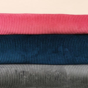 Könnte beinhalten: Drei Rollen Cordstoff in Pink, Blau und Grau.