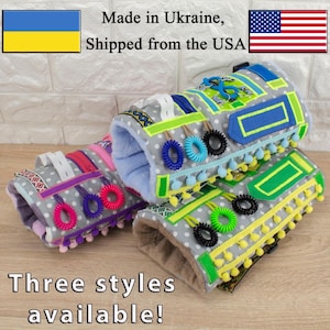 May include: Three different styles of sensory activity wrist cuffs for babies and toddlers. Each cuff features a variety of textures, colors, and shapes, including zippers, buttons, ribbons, and elastic bands. The cuffs are made of soft, durable fabric and are designed to help develop fine motor skills and sensory exploration.