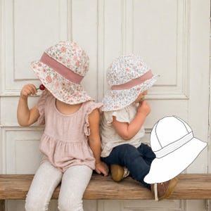 Könnte beinhalten: Zwei Kinder tragen Sonnenhüte mit floralem Muster, breiter Krempe und rosa Band. Die Hüte haben einen hellen Hintergrund mit einem Muster aus kleinen Blumen. Die Kinder sitzen auf einer Holzbank.