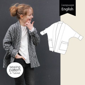 Könnte beinhalten: Ein grauer Cardigan mit weißem Muster und zwei Taschen. Der Cardigan ist offen und ein Kind trägt ihn. Das Bild zeigt auch eine Strichzeichnung des Cardigans.