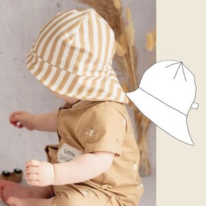 Könnte beinhalten: Ein Baby trägt einen braunen und weißen gestreiften Sonnenhut mit dem Text "Little Sunshine" auf der Vorderseite. Der Hut hat eine breite Krempe und ist aus einem weichen, atmungsaktiven Stoff gefertigt. Das Baby trägt einen braunen Overall mit Blumenmuster.