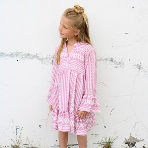 Puede incluir: Un vestido de rayas rosa y blancas con un patr&oacute;n geom&eacute;trico blanco. El vestido tiene mangas largas con pu&ntilde;os acampanados y una falda de capas.