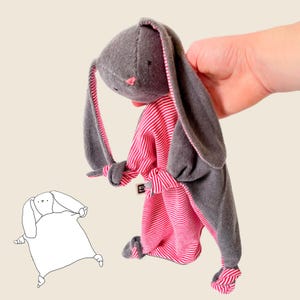 May include: A gray and pink bunny plush toy with long ears. The bunny is wearing a pink and white striped outfit with a gray sash.