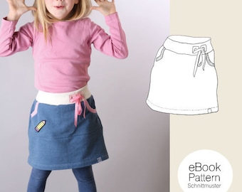 May include: A girl wearing a pink long-sleeved shirt and a blue denim skirt with a white waistband and pink ribbon. The skirt has a yellow pencil design on the front. The image also shows a line drawing of a skirt with a drawstring.