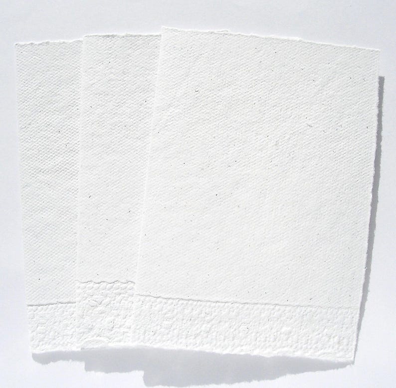 3 weiße Klappkarten aus handgeschöpftem Papier mit geprägtem Spitzenrand an der unteren Seite von paperuli liegen im Hochformat fächerförmig auf dem Tisch.