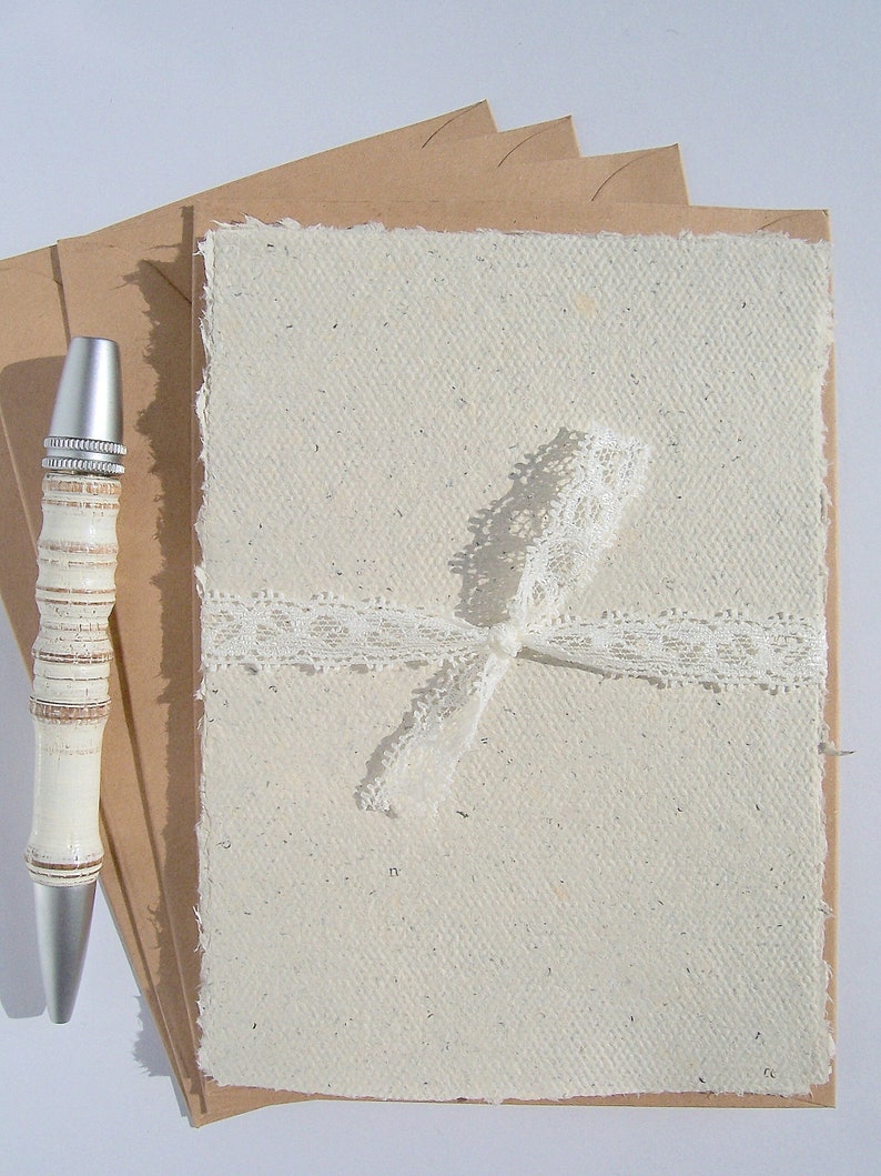 4Büttenpapier-Postkarten mit echtem Büttenrand von paperuli, mit Spitzenband auf 4 Kraftpapier-Umschläge gebunden, daneben ein Kugelschreiber zur Veranschaulichung der Größe